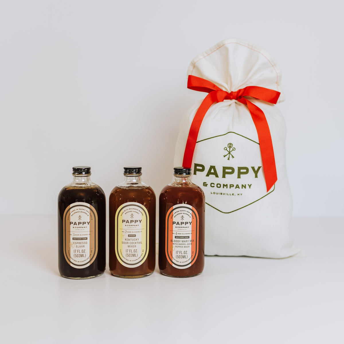 Three Pappy and Company mixers lined up next to a white bag with a red ribbon